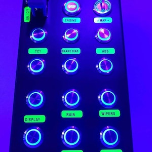 Puede incluir: Un panel negro con una variedad de botones iluminados, incluyendo "Motor", "TC1", "Freno de mano", "ABS", "Lluvia", "Limpiaparabrisas", "Pantalla", "Luces" y "Limitador". El panel también cuenta con un interruptor de palanca etiquetado como "ON/OFF" y un botón más pequeño etiquetado como "IGN". El panel está etiquetado como "XBOX" en la esquina superior derecha.