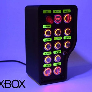 Op de afbeelding: Een zwart bedieningspaneel met een verscheidenheid aan knoppen en labels, waaronder "IGN", "START", "WIPERS", "LIGHTS", "FLASH", "-TCC+", "BIAS+", "-MAP+", "MOTOR START", "-ABS+", "DISPLAY", "LIMITER". Het paneel is verlicht met verschillende gekleurde lampjes.