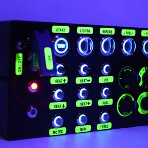 May include: A black panel with green and white labels and buttons. The labels read "START", "LIGHTS", "WIPERS", "-FUEL", "-FOV+", "SEAT+", "SEAT", "PIT", "ABS", "SEAT", "SEAT+", "FUEL", "DISP", "MOTEC", "MFD", and "TYRES".
