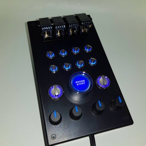 May include: Black control panel with multiple blue illuminated buttons, a large round blue illuminated button labeled "ENGINE START", and four black knobs with blue accents.