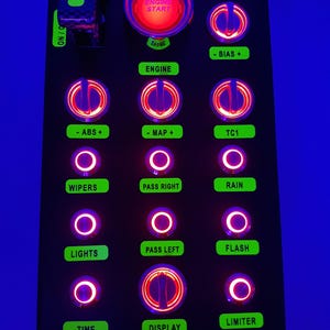 May include: A black panel with a variety of illuminated toggle switches and buttons. The switches are labeled with text such as "Engine Start", "ABS", "MAP", "TC1", "Wipers", "Pass Right", "Rain", "Lights", "Pass Left", "Flash", "Limiter", "Time", and "Display".