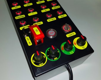 May include: A black control panel with various buttons and switches, including a red "Engine Start" button, a red "IGN" toggle switch, and a black "Lights" toggle switch. The panel also features a black and yellow "TC" knob, a black and green "TC2" knob, a black and green "ABS" knob, and a black and green "BIAS" knob.