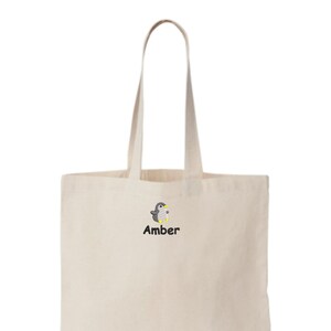 May include: A beige tote bag with a black embroidered penguin and the name "Amber" underneath.