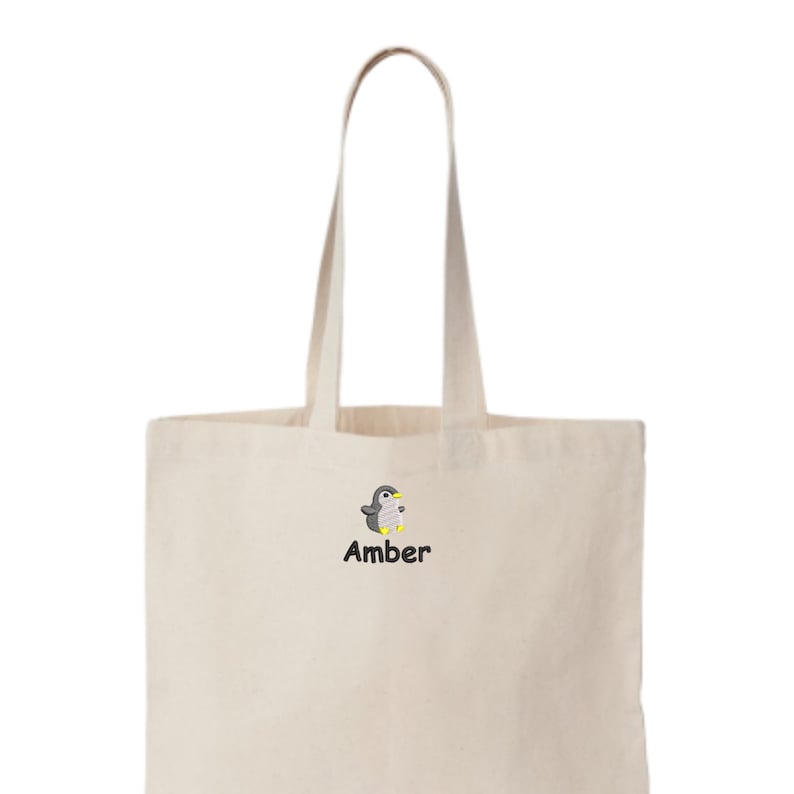 May include: A beige tote bag with a black embroidered penguin and the name "Amber" underneath.