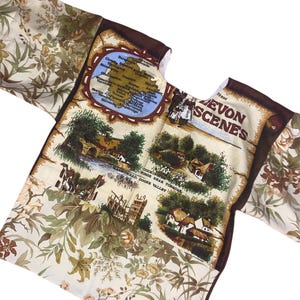 May include: A brown and white fabric with a map of Devon, England and images of Devon scenes. The text "First Devon Scenes" is printed on the fabric.