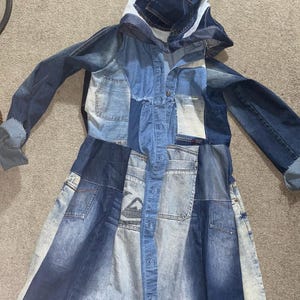 May include: A long denim coat with a patchwork design. The coat features a hood and is constructed from various shades of blue denim. It has a button-up front and pockets, showcasing a unique, upcycled aesthetic.