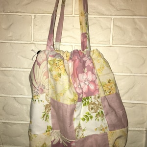 May include: A pink and yellow floral patchwork tote bag with a drawstring closure. The bag has a patchwork design with different floral patterns and colours.