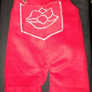 May include: Red corduroy dungarees with a white embroidered heart on the front pocket.