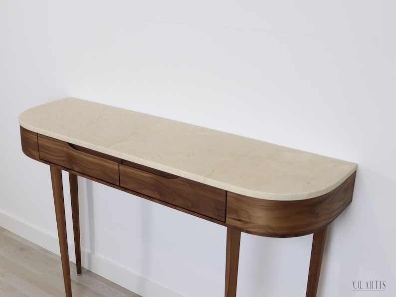 May include: A modern console table with a curved top made of walnut wood and a cream-colored marble top. The table has two drawers and four slender legs.