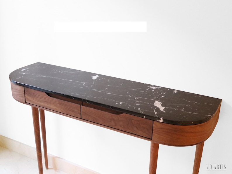May include: A curved walnut wood console table with two drawers and black marble top. The table has four slender legs.