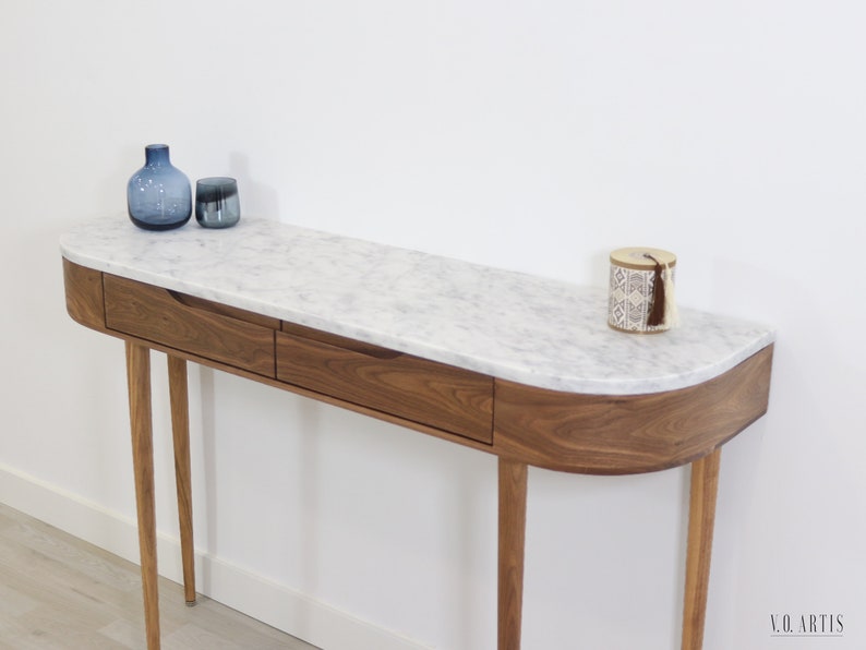 May include: A modern console table with a white marble top and two drawers. The table has a curved front edge and is supported by four slender wooden legs.