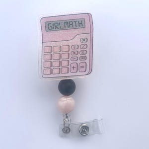 Peut inclure: Un badge enrouleur de calculatrice rose pailleté avec le texte "GIRLMATH" affiché à l'écran. Le badge enrouleur a un accent de perles noires et roses et un clip en plastique transparent.