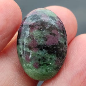 Könnte beinhalten: Ein ovaler Edelstein mit glatter, polierter Oberfläche in den Farben Grün, Schwarz und Rosa.