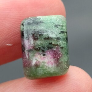 Könnte beinhalten: Ein grüner und rosafarbener Edelstein-Cabochon mit einem einzigartigen Muster. Der Stein hat eine raue, strukturierte Oberfläche und ist ein wunderschönes Beispiel für natürliche Schönheit.