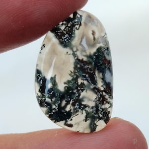 May include: A smooth, white agate cabochon with a dendritic pattern of black and green inclusions. The stone is translucent and has a natural, organic shape.