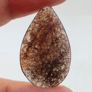 Pode incluir: Um cabochão de ágata marrom translúcida em forma de lágrima com um padrão salpicado.
