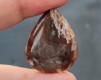 May include: A teardrop-shaped, translucent brown agate cabochon with white and brown inclusions. The stone has a polished, smooth surface.