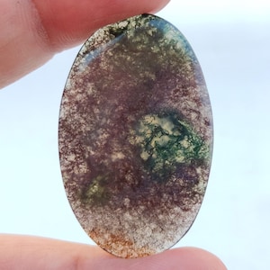 Pode incluir: Um cabochão de ágata verde, marrom e branco com um padrão de redemoinho. O cabochão tem formato oval e uma superfície lisa e polida.