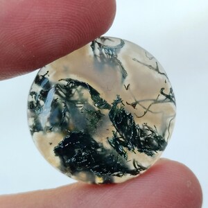 May include: A round, translucent agate cabochon with a dendritic pattern of green and black inclusions. The agate has a white and gray background.