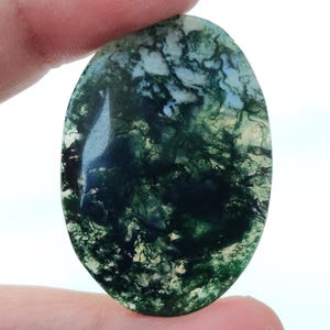 May include: A green and white moss agate cabochon with a swirling pattern. The stone is oval shaped and has a smooth, polished surface.