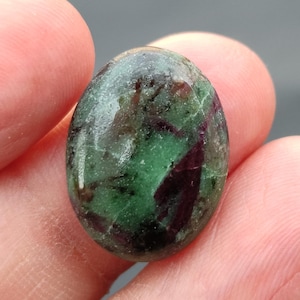 Könnte beinhalten: Ovaler grüner und violetter Edelstein mit einer glatten, polierten Oberfläche. Der Stein hat eine marmorierte Optik mit grünen, violetten und weißen Wirbeln.