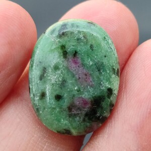 Könnte beinhalten: Ein ovaler Edelstein in Grün und Pink mit schwarzen Flecken. Der Stein ist glatt und poliert.