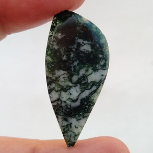 May include: A green and white moss agate cabochon with a teardrop shape. The stone has a swirling pattern of green and white.