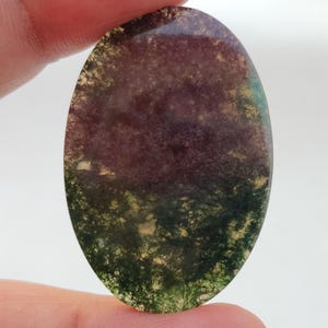 Pode incluir: Uma gema oval cabochão com um padrão de redemoinho em tons de verde, marrom e roxo.