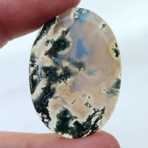 May include: Oval shaped green moss agate cabochon with a white and gray background. The stone has a natural, organic pattern.