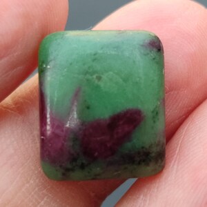 Könnte beinhalten: Ein grüner und violetter Edelstein mit quadratischer Form. Der Edelstein hat eine glatte, polierte Oberfläche.