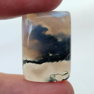 May include: A rectangular, translucent, light gray agate cabochon with dark gray and green dendritic patterns.