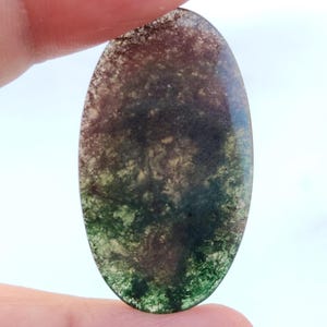 Pode incluir: Cabochão de ágata ovalado de cor verde, marrom e branco com um padrão de redemoinho.