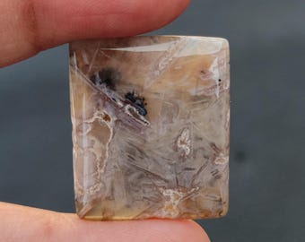 May include: A rectangular, light brown agate cabochon with a white and grey pattern. The stone has a smooth, polished surface and is translucent.
