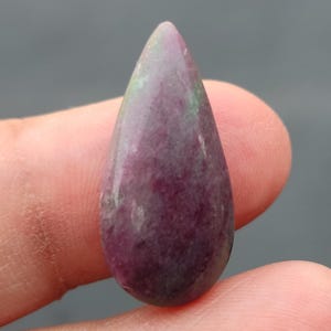 Op de afbeelding: Een traanvormige cabochon edelsteen met een paarse en groene kleur.