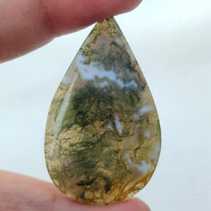 May include: A teardrop-shaped green, white, and brown agate cabochon with a swirling pattern.