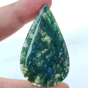 May include: A green and white moss agate cabochon with a teardrop shape. The stone has a natural, organic pattern.