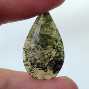 May include: A teardrop-shaped green moss agate cabochon with a white and green pattern. The stone is translucent and has a natural, organic look.