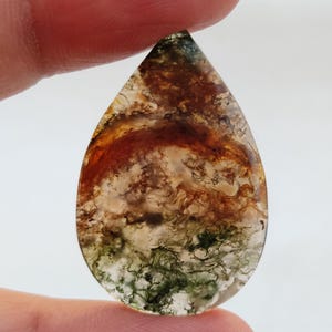 May include: A teardrop-shaped agate cabochon with a brown, green, and white pattern. The stone has a natural, organic look.