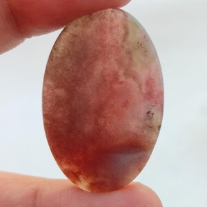 May include: A smooth, oval-shaped cabochon gemstone with a swirling pattern of red, brown, and white.