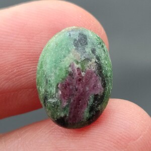 Könnte beinhalten: Ein ovaler Edelstein in Grün- und Rosatönen mit einem einzigartigen Muster. Der Edelstein ist im Cabochon-Schliff geschliffen.