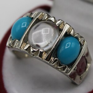May include: A silver ring with three stones. The center stone is clear and round. The two stones on either side are turquoise and round.