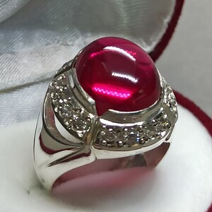 May include: A silver ring with a large, oval-shaped, red gemstone surrounded by smaller, white gemstones.