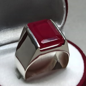 Könnte beinhalten: Ein silberner Ring mit einem großen, rechteckigen, tief roten Edelstein.