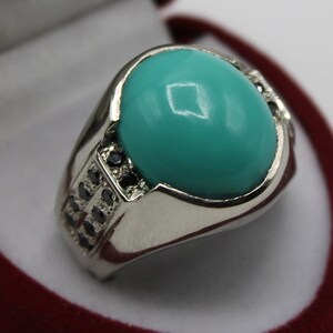 May include: A silver ring with a large turquoise stone and smaller black stones set in the band.