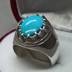 May include: A silver ring with a turquoise stone set in a decorative silver bezel. The ring is on a white surface.