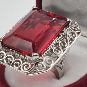 May include: A silver ring with a large, red, rectangular gemstone set in a filigree design.
