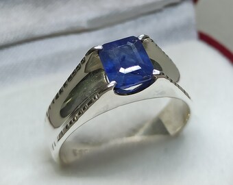 May include: A silver ring with a blue gemstone set in a square shape. The ring has a textured band.