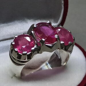 Könnte beinhalten: Ein silberner Ring mit drei ovalen rosafarbenen Edelsteinen. Der Ring ist in einer silbernen Band mit einem strukturierten Design gefasst.