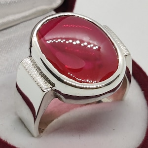 May include: A silver ring featuring a large, oval-shaped, bright red gemstone.