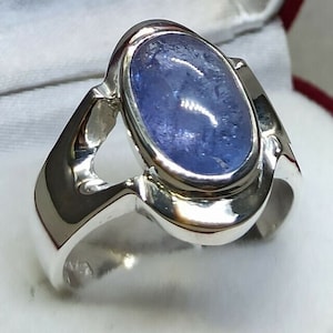 May include: A silver ring featuring a blue oval gemstone set in a bezel setting. The ring has a distinctive design with a curved band and a cutout on the side.